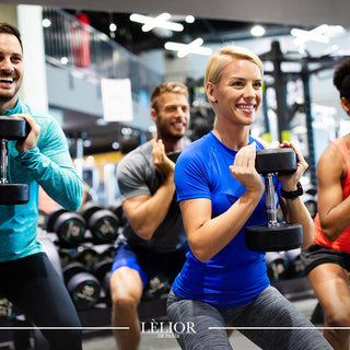 Two men and two women holding dumbells, squatting and working out in the gym